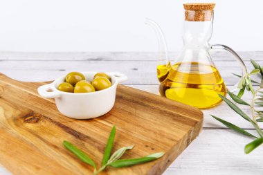Dolu bir şişe zeytin yağı, yeşil ve siyah zeytin ve ahşap bir tahtada zeytin filizi, beyaz arka plan..