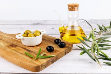 Altın zeytin yağıyla dolu bir şişe. Köy tahtası ve beyaz bir taban üzerinde zeytin ve dalların yanında..