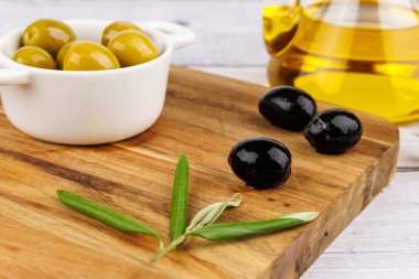 Yanında yeşil ve siyah zeytinlikler ve tahta üzerinde zeytin dalları, beyaz arka plan..