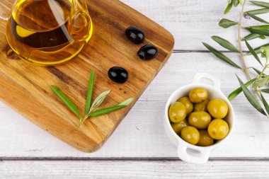 Ahşap bir zemin ve beyaz zemin üzerinde zeytin ve filizlerle dolu zeytin yağı şişesi..