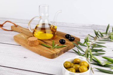 Taze zeytin yağı şişesi ve ahşap tahtada doğal zeytin filizi, beyaz yüzey.