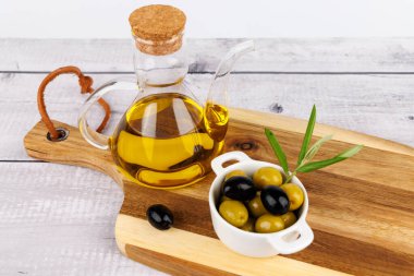 Siyah ve yeşil zeytinli organik zeytinyağı şişesi, ahşap tahtada zeytin yaprakları ve temiz arka plan.
