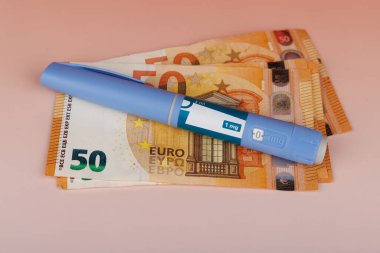 Kırmızı bir arkaplan üzerindeki banknotlar üzerindeki semaglutid kalemlerin yatay görüntüsü diyabet veya obezite tedavisinin maliyetini temsil etmektedir.