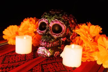 Kültürel sunak, çiçeklerle süslenmiş siyah bir kafatası, parlak mumlar ve tekstil arka planında manolyalar gösterir..