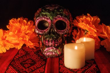 Dia de los Muertos sırasında Meksika tekstili üzerinde çiçekli bir kafatası, yanan mumlar ve manolyalar gösteren bir sunak..