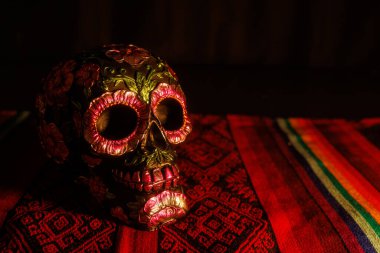 Ölüler Günü 'nde Meksika sunağının bir parçası olan folklorik bir örtüde çiçeklerle süslenmiş siyah kafatası..