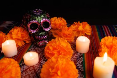 Geleneksel bir sunakta metal çiçekler ve manolyalarla süslenmiş siyah bir kafatası etrafında parlayan mumlar..