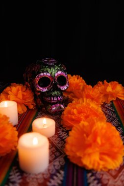 Renkli mumlar ve manolyalar ile çevrili metal çiçekli siyah kafatası sunağı.