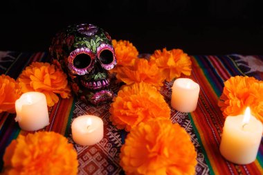 Parlak mumlar Dia de Muertos için manolyalarla süslenmiş geleneksel bir sunakta siyah bir çiçek kafatası yakar..