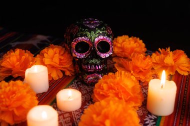 Beyaz mumlar ve manolyalar ile çevrili metalik çiçeklerle süslenmiş seramik siyah kafatası..