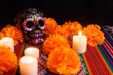 Aydınlatılmış siyah kafatası. Metalik çiçekler, beyaz mumlar ve manolyalar. Ölüleri onurlandırmak için geleneksel bir beze konulmuş..