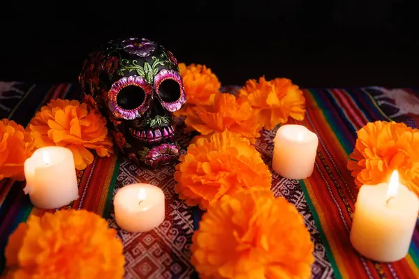 Parlak mumlar Dia de Muertos için manolyalarla süslenmiş geleneksel bir sunakta siyah bir çiçek kafatası yakar..