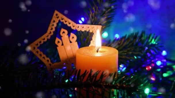 点着的橙色蜡烛点着圣诞装饰品 绿色的枞树枝条和下着雪的效果 圣诞气氛 — 图库视频影像