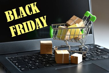 Alışveriş arabası, paketler ve Kara Cuma 'lı dizüstü bilgisayar ekranda yazıyor. Çevrimiçi alışveriş ve Kara Cuma kavramı