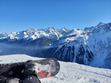 Büyüleyici bir dağ manzarasının önünde dinlenen bir snowboardcu.