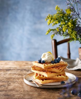 Üzerinde yabanmersini, dondurma ve bal olan waffle 'lar kırsal kahverengi bir masada duruyor. Mavi arka plan. Fazladan yeri olan sakin bir hayat. Minimalist kompozisyon. Kopyalamak için boşluk.