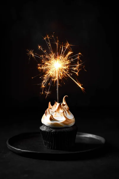 Tek çikolatalı kek ve kremalı pasta. Kekin içinde maytap. Siyah arka plan, tabak ve taş masa. Huysuz hayat. 