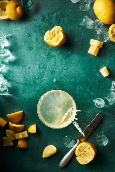 Etrafı buz, su sıçraması ve limonlarla çevrili deniz mavisi arkaplanındaki turunçgil kokteyli. Bazı limonlar zaten sıkılmış. Hazırlık ve malzeme görüntüsü. Ferahlatıcı bir his. Üst görünüm dikey düz resim. 