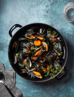 Buharda pişmiş ve siyah tencerede midye yemeye hazır. Mavi desenli arka plan. Bir bardak su, kaşık ve peçete.. 