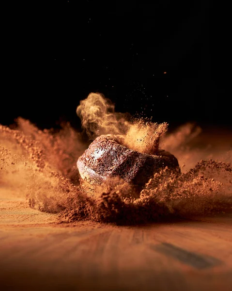 Kakao tozunun içine düşen mini çikolatalı kek. Kakao tozu merminin etrafında her yere yayılıyor. Keskin hareket yakalandı. Koyu siyah arkaplan. 