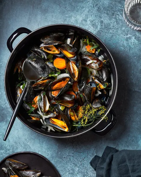 Buharda pişmiş ve siyah tencerede midye yemeye hazır. Koyu mavi desenli arka plan. Bir bardak su, kaşık ve peçete.. 