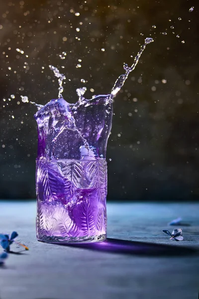 Kelebek bezelye çayı ve limonlu mor kokteyl. Çok heyecan verici bir sıçrama var. Koyu mavi taş masa ve siyah arka plan. Arka planda çiçekler var. Donmuş hareketli yaşam tarzı resmi. 