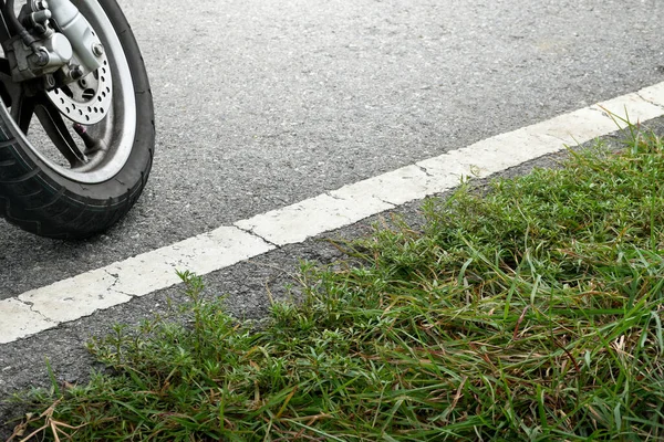 Motorcycle wheels are on the road and grass background,soft sunlight,car wheels and traffic lines on the road,car braking system,cars on the road,close up.