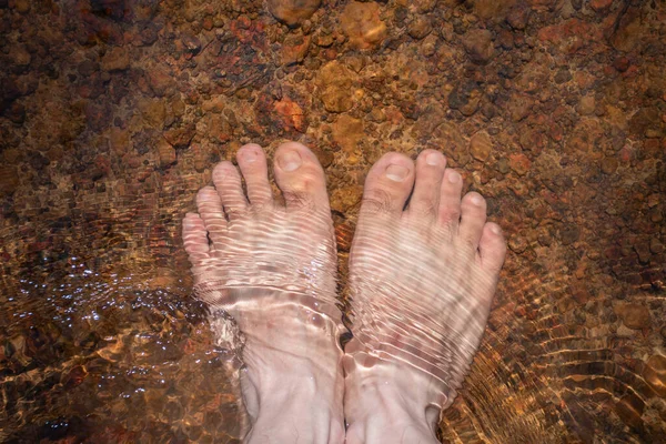 Top view feet in the water In the clear river, foot soaked in the water on the background of water and ground surfaces,natural mineral water, clear water waves,foot spa,health care,close up,relax,holiday