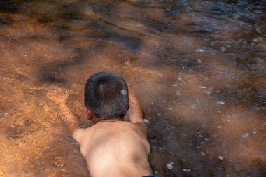 Asyalı genç tatlı bir çocuk arka planda, su yüzeyinde ve gündoğumlarında nehirde yüzen sevimli ve büyüleyici bir su, su oynayan çocuk, Asyalı çocukların yaşam tarzı, yaşam ve sürdürülebilirlik kavramı..