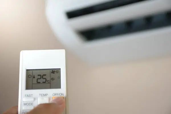 Beyaz odadaki klimayı 25 derecede açmak için uzaktan kumandayı tutarken, arka plandaki elektrik ve elektrik cihazlarını korumak için yumuşak güneş ışığı kavramı bulanıklaştı..