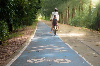 Yolda bisiklet süren iki Asyalı genç çocuk ve bisiklet sembolü çam ormanının ortasında açık hava parkı manzarası arkasında aktivite ve sağlıklı konsept için..