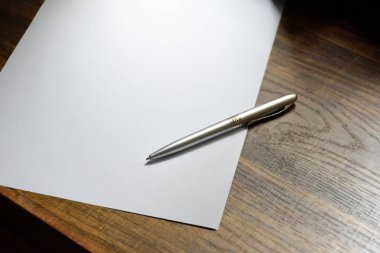 Alüminyum kalem ve boş kağıt not almak ya da ofiste çalışmak için ahşap desenli bir masaya yerleştirilir..