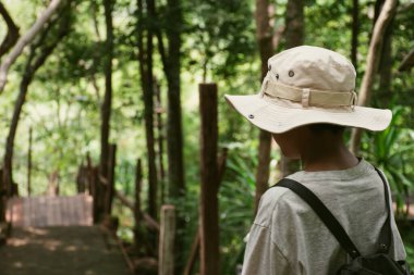 Arka planda dağ ormanında yürüyüş şapkası ve köprü çantası takan bir adamın yakın çekimi..