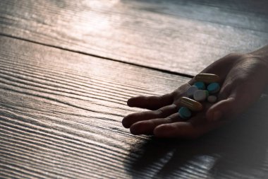 Aşırı dozda uyuşturucu kullanımı ve uyuşturucu kullanımının tehlikeleri için tahta zemin üzerinde ilaç hapları tutan eller. Elimizde çeşitli ilaç türleri var..