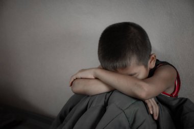 Yakın plan çocuğu, siyah bir yatak odasında dizleri üzerinde oturur ve aile içi şiddetten ve çocukluk zorbalığından dolayı üzgün ve depresif hisseder..