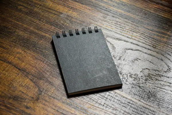 Küçük siyah defter, not almak ya da yazmak için ahşap desenli bir masaya oturur..