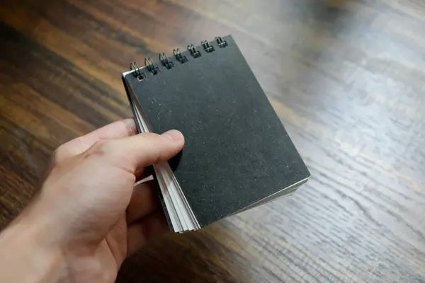 İşadamı elinde küçük siyah bir defter tutuyor. Ofiste masa başı ahşap desen..