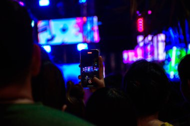 Akıllı telefonun el ele tutuşması, arka planı bulanık renkli spot ışıklarıyla bir konserin videosunu kaydediyor..