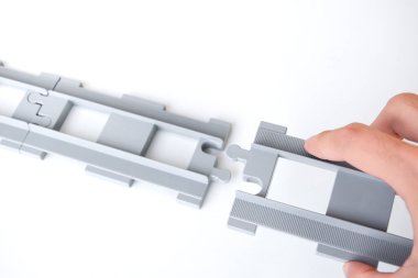 Beyaz bir arka plana yerleştirilmiş gri oyuncak demiryolu rayları. Bağlantı konsepti ve bağlantıyı kesmek için onları birbirine bağlayan tpy demiryolu raylarını tutan el..