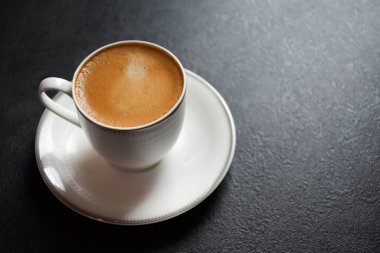 Sıcak espresso kahvenin en üst görüntüsü ya da siyah arka plan 2024 'te beyaz cam bir fincanda Amerikano. Siyah masanın üzerinde güzel beyaz bir fincan kahve..