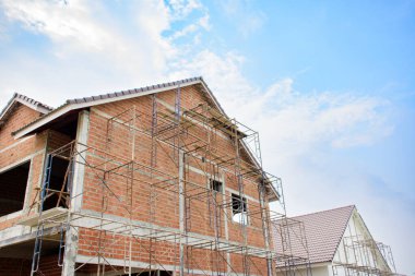 Modern evler ve konut konsepti 2025 olan kahverengi inşaat alanı. Mavi gökyüzü arkaplanına karşı inşaat ve inşaat çalışmaları devam ediyor.