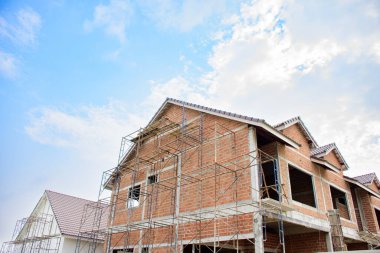 Modern evler ve konut konsepti 2025 olan kahverengi inşaat alanı. Mavi gökyüzü arkaplanına karşı inşaat ve inşaat çalışmaları devam ediyor.