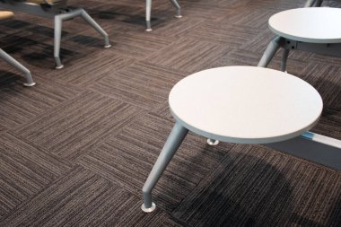 Siyah halı arka planında havaalanına bagaj yerleştirmek için beyaz, yuvarlak ahşap kalaslar. Beyaz sandalyeler ve kapalı masa. Modern konforlu plastik mobilyalar.