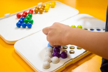 Çocuk elinin sarı arka planda Jumbo boncukları oynaması, 3 boyutlu mantık IQ boncukları bulmacası oynayan çocuklar, öğrenme ve beceriler için sınıfta renkli bulmaca boncuklarıyla oynayan çocuklar..