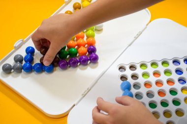 Çocuk elinin sarı arka planda Jumbo boncukları oynaması, 3 boyutlu mantık IQ boncukları bulmacası oynayan çocuklar, öğrenme ve beceriler için sınıfta renkli bulmaca boncuklarıyla oynayan çocuklar..