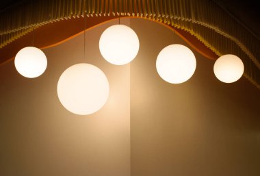 Modern evde kahverengi duvarlı, modern tavan lambasını kapatan bir lamba seti. Minimalist iç mekan 2024 'ün sıcak tonlarında dairesel ampullerle süslenmiştir.. 