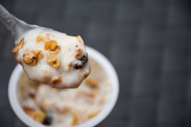 Yoğurt ve mısır gevreği, tam tahıl, granola, müsli kaşıkta siyah bulanık arkaplan. Sağlıklı bir kahvaltı için mısır gevreğiyle birlikte beyaz yoğurt yakın..