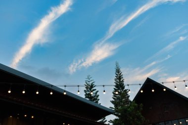 Çağdaş çiftlik evinin çatısı, mavi gökyüzü günbatımına karşı arka planda, modern kafenin içi, sıcak renklerde aydınlatma, günbatımı gökyüzü ve modern ev kuleleri..