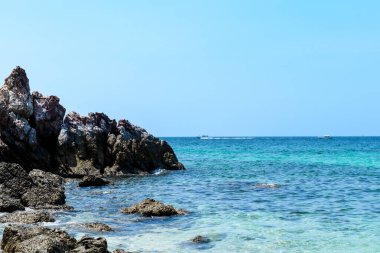 Berrak mavi sularda kayaları olan tropikal bir plajın manzarası ve Koh Larn adasındaki açık bir gökyüzünde sabah dalgalar. Panorama Okyanusu. Pattaya, Tayland