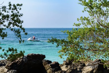 Mavi denizde jet ski süren ve açık mavi gökyüzünde kayalar olan bir adam ve Koh Larn Adası 'ndaki arka plan sabahı. Panorama Okyanusu. Pattaya, Tayland. Dalga, Tatil, Deniz Burnu, Aktivite, Tekne.